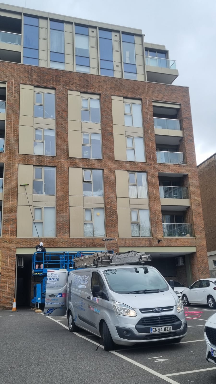 Sam and Son van beside a lift platform while windows on a high-rise block are cleaned with a pole